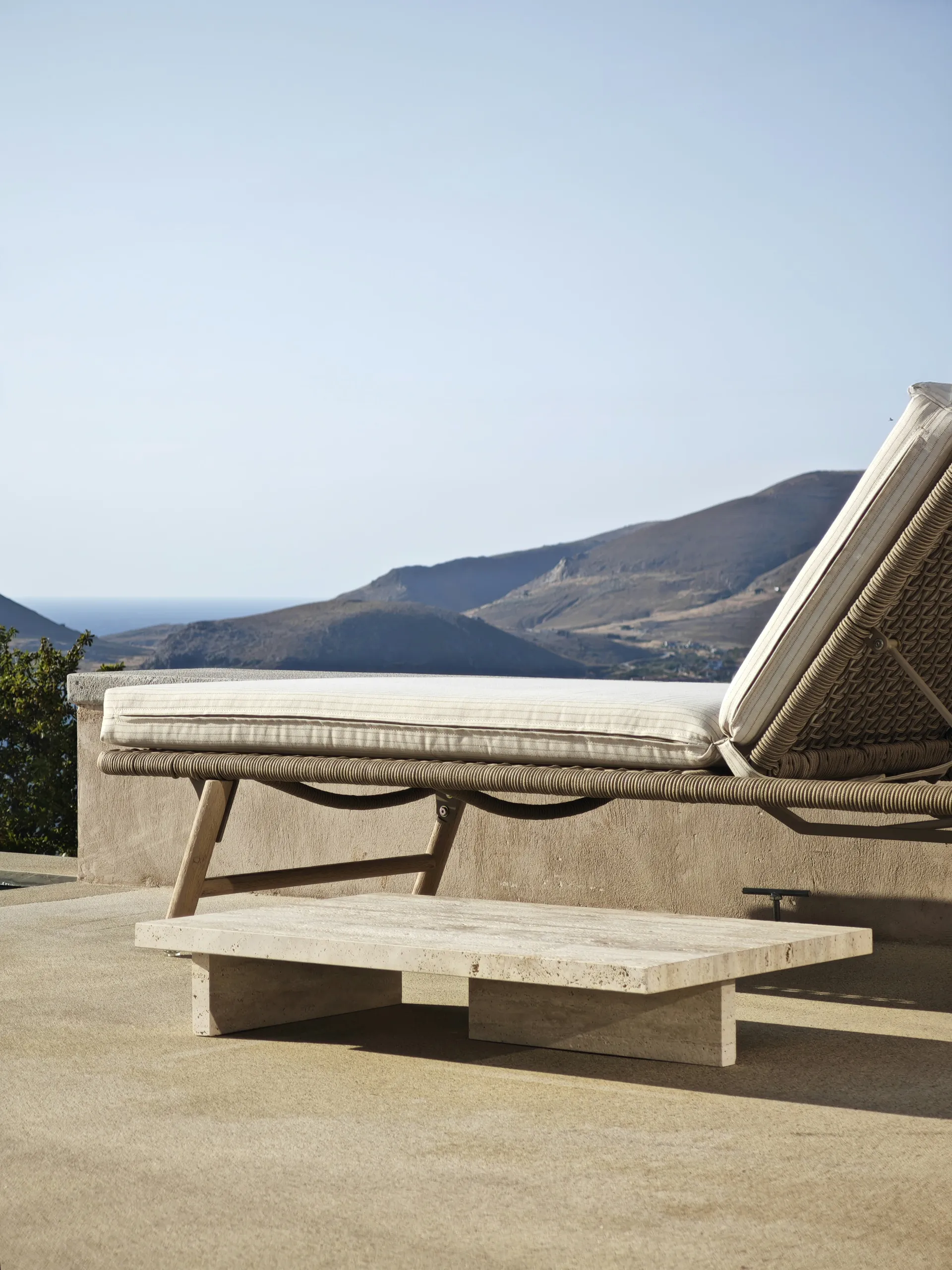 Low rectangular travertine table beside a woven outdoor lounger